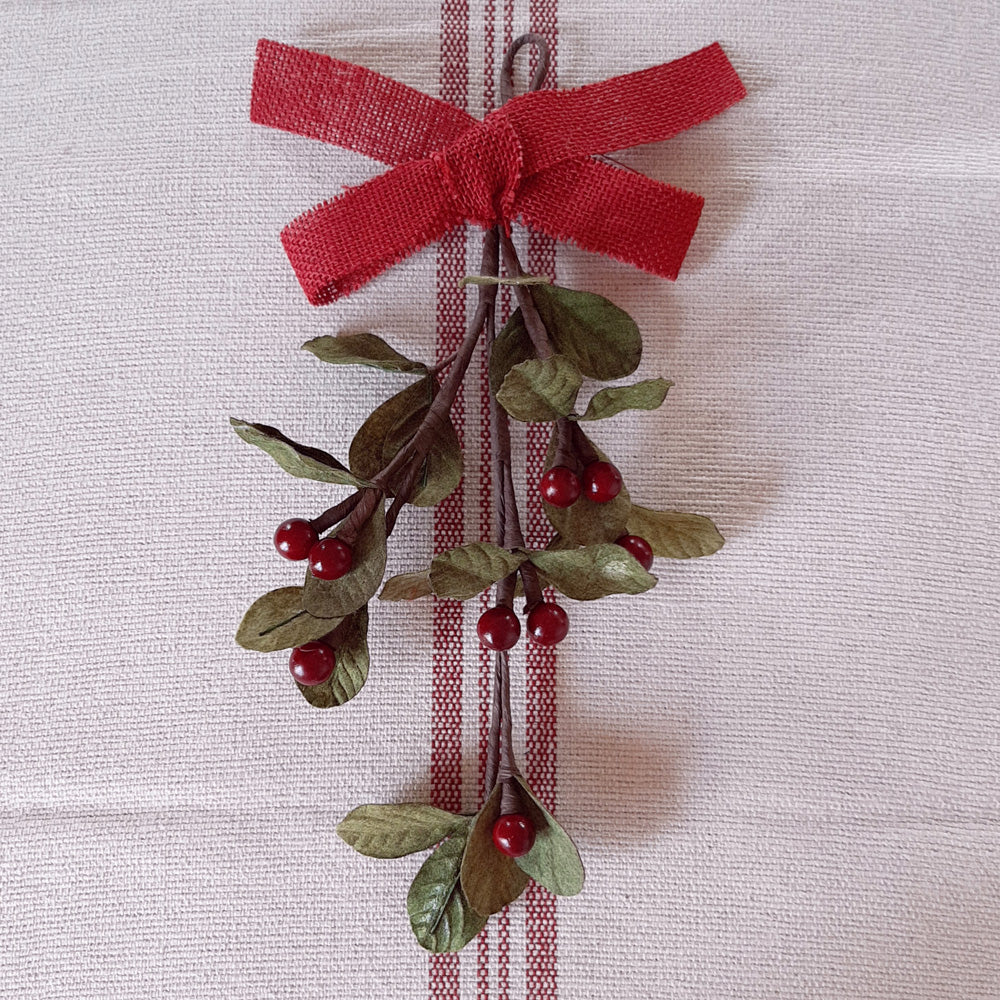 The Mistletoe and Berry Teardrop will surely inspire a kiss or two. This charming faux floral display can hang on a door or wall. Featuring deep red/burgundy berries and vibrant green mistletoe leaves and a red burlap bow. Measures 12" H