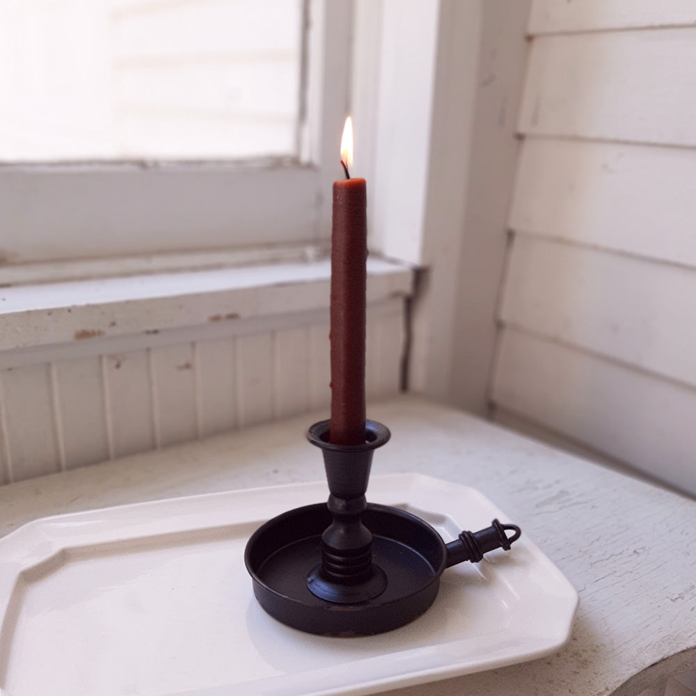 The Old Colonial Candlestick Holder adds an antique ambiance to any room. This chamberstick style candle holder features a distressed black finish with raised neck and a shallow pan for catching wax drippings. Taper candle not included. This piece makes a simple yet charming accent to any room in your farmhouse.