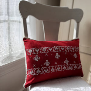 The Scandi Cottage Embroidered Pillow lends a cheerful vintage touch to any room. This beautifully hand embroidered Scandinavian-inspired accent pillow features bright white embroidery against a red background with crochet lace trim. The back features a classic plaid with a button closure. 100% cotton. Includes insert. 18"L x 12"H