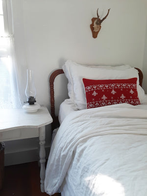 The Scandi Cottage Embroidered Pillow lends a cheerful vintage touch to any room. This beautifully hand embroidered Scandinavian-inspired accent pillow features bright white embroidery against a red background with crochet lace trim. The back features a classic plaid with a button closure. 100% cotton. Includes insert. 18"L x 12"H