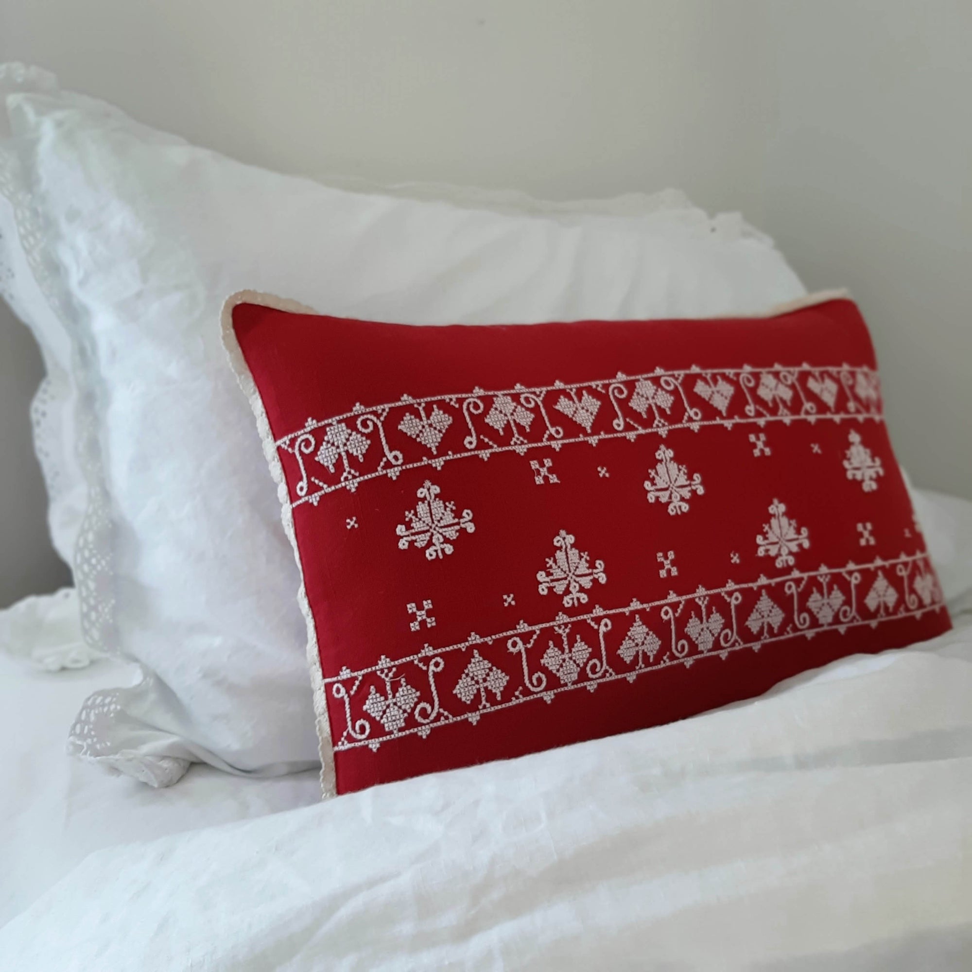 The Scandi Cottage Embroidered Pillow lends a cheerful vintage touch to any room. This beautifully hand embroidered Scandinavian-inspired accent pillow features bright white embroidery against a red background with crochet lace trim. The back features a classic plaid with a button closure. 100% cotton. Includes insert. 18"L x 12"H