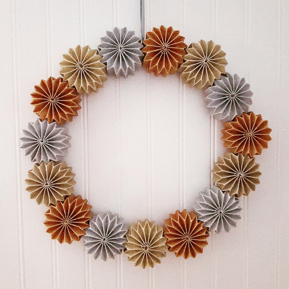 This handmade Sparkle Paper Pinwheel Wreath is an eye-catching and unique holiday accent. The chunky paper pinwheel style flowers sparkle with a combination of glittery gold, silver and copper. The wreath is topped off with a silvery-grey ribbon for hanging. This charming wreath lends a down-to-earth, handmade feel to your holiday home. Made with heavy-duty cardboard. For indoor use only.  15" diam