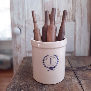 This handsome Stoneware Crock is inspired by early 20th century pottery found in farmhouses throughout the US. This reproduction crock has an oatmeal color with a blue White Cottage Stoneware Co. logo, making this piece a perfect accent for American farmhouse style kitchens. Use to store cooking utensils or display your favorite flowers. (Rolling Pins and Flowers not included) 5.75” Diam x 7”H