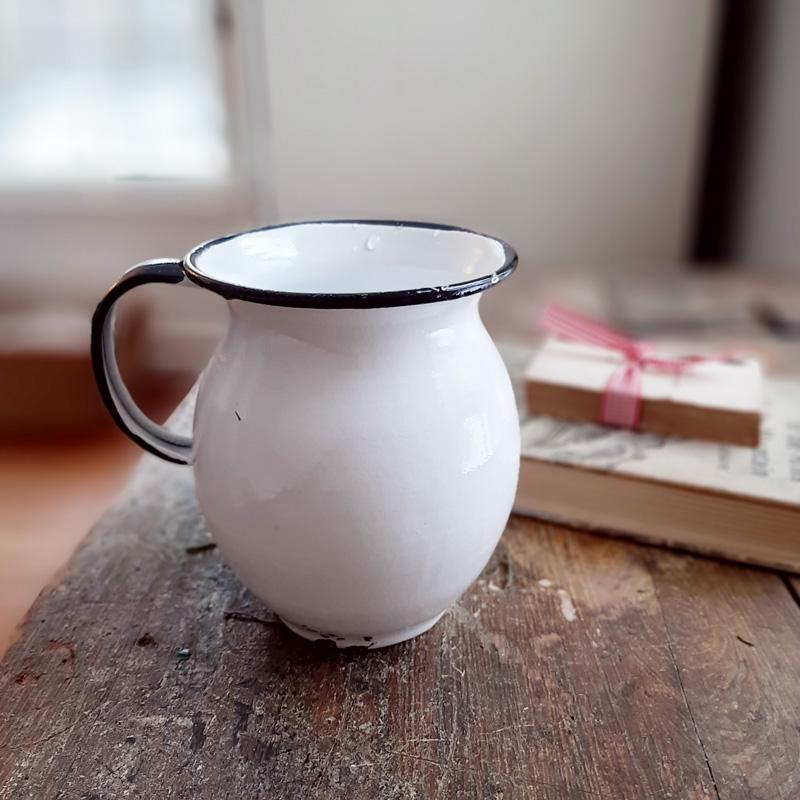 Bring the easy charm of country cottage living to your farmhouse with our White Enamel Pitcher with Vintage Style. The simple allure of enamelware fits right in with any decor, but every farmhouse needs at least one piece. Inspired by flea market finds, our white enamel pitcher has black trim and makes the perfect vase for your favorite bouquet. Not food safe.