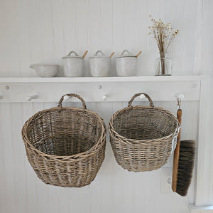 Wicker lends easy charm to any room with its earthy, neutral shades and woven texture. Our Wicker Wall Baskets, made of woven willow,  have a vintage cottage feel to them, and they offer relaxed farmhouse elegance to any room. Ideal for creating a welcoming basket of flowers on a vintage style porch or use for storage in a rustic farm kitchen. Features a faint grey wash for an aged look. Set of two. 10X7X9(S) 9.5X9X12(L)